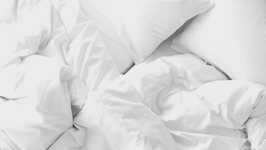 An image of an unmade bed with white molecule bed sheet.