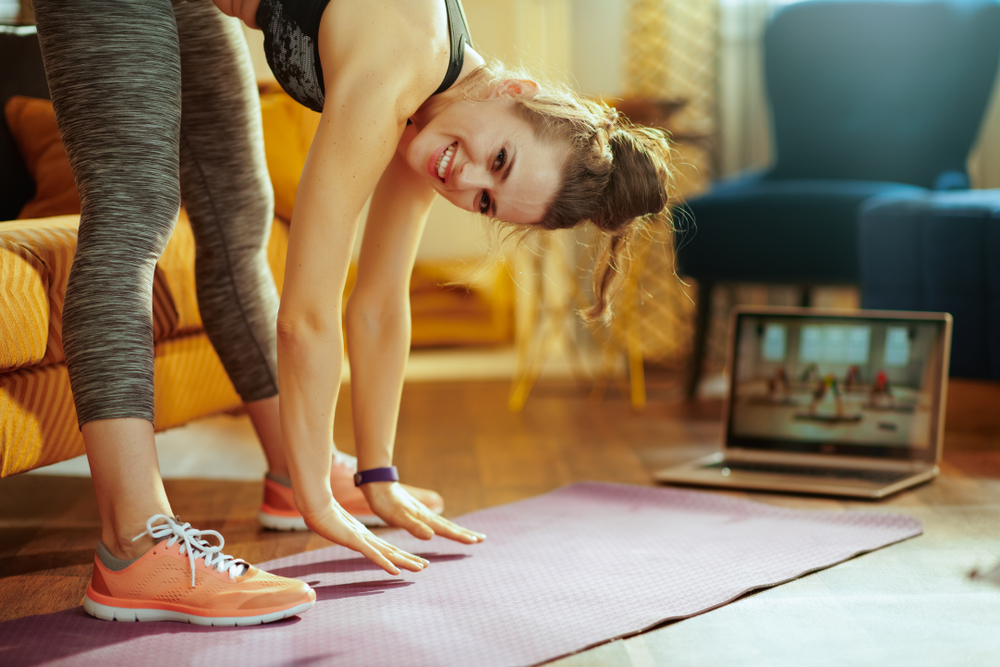 Fit woman working out at home while watching an online course which is one of the virtual training platforms today.
