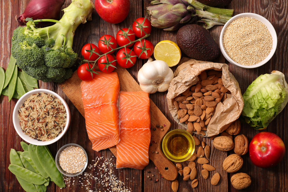 Healthy food like salmon, broccoli, tomatoes, nuts, avocado, lettuce on a wooden surface. Make sure you have enough vitamins and supplements in your diet.