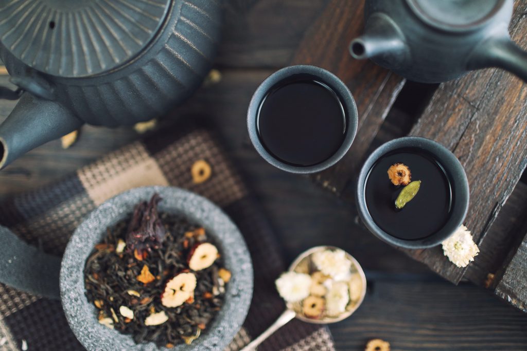 Top view image of two cups of tea and two pots with some seeds on the side.