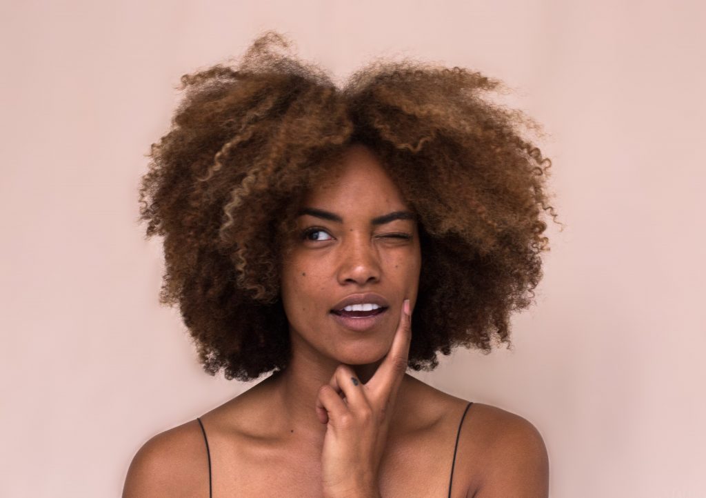 An Afro American woman feeling her face thinking of tips for clear skin.