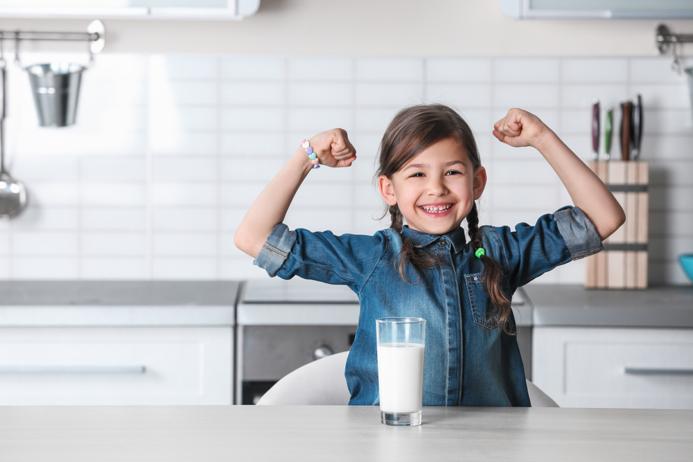 Little girl flexing muscles on both arms after drinking milk, as a sign that she's stronger.
