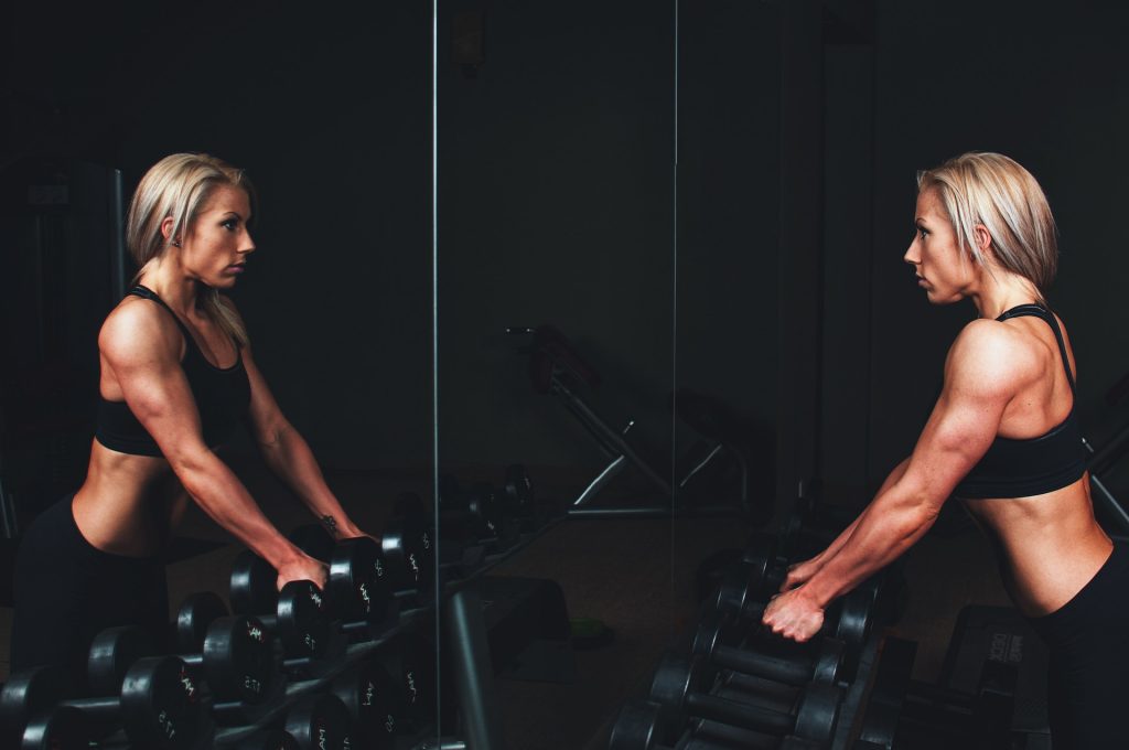 A fit woman facing a mirror trying to lift a dumbbell. Healthy Habits for your lifestyle to increase your fitness