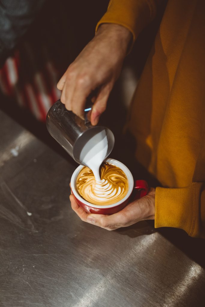 Person pouring milk foam into a cup of coffee. You have to try these healthy hot drinks at Starbucks.