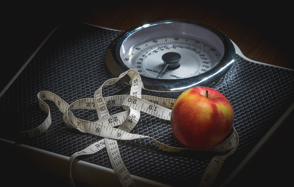 An apple and a tape measure on the top of a bathroom scale to illustrate weight loss strategies