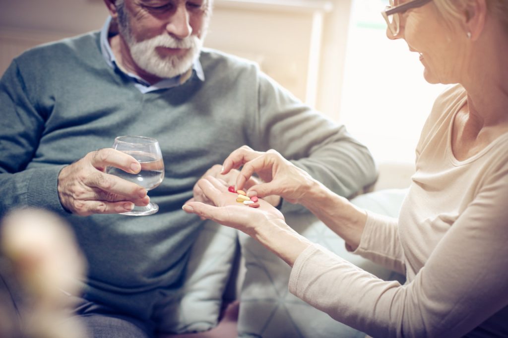 Senior woman giving her husband medication vitamins supplement.