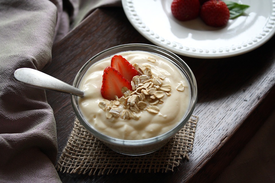 Yogurt in a bowl with strawberry and outs on top on a wooden table.