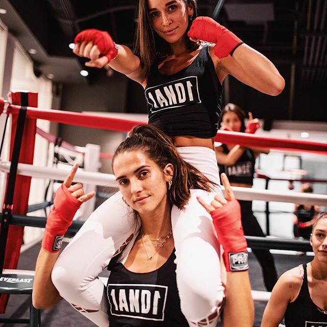 Amanda Carola and Amanda Riley striking poses next to a boxing ring.