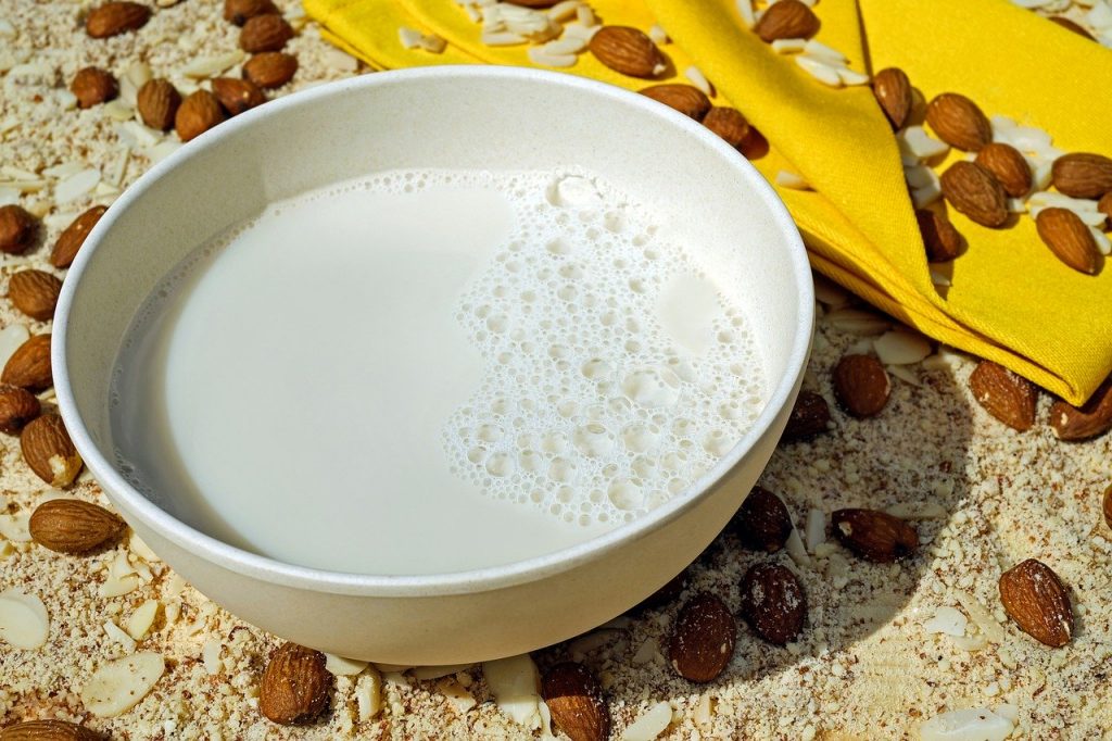 A bowl of almond milk surrounded by scattered almonds.