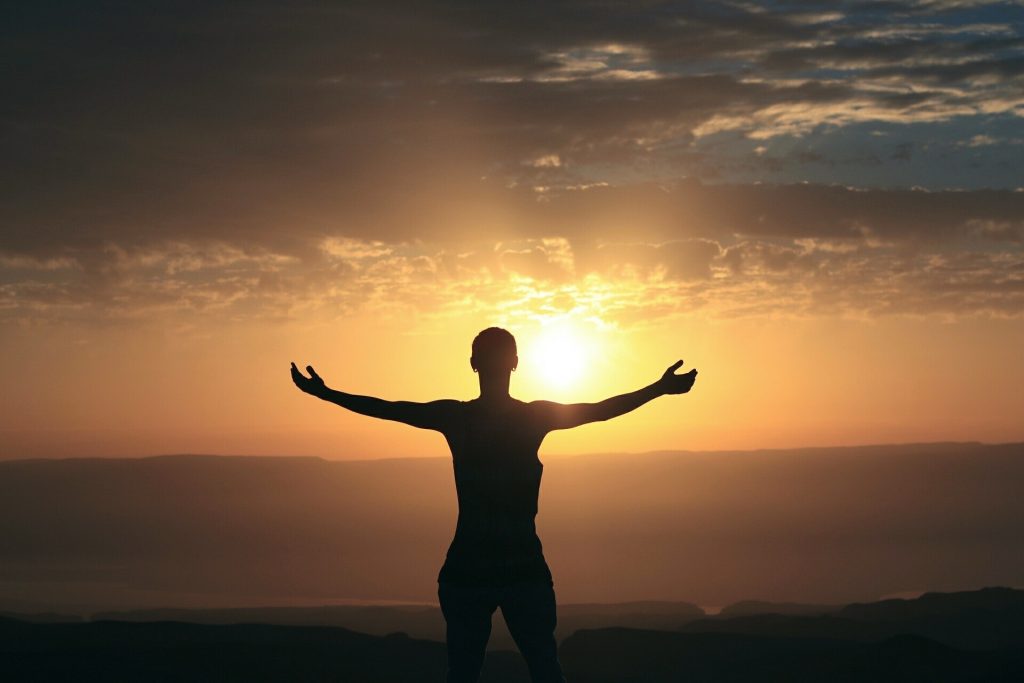 Man with open arms looking at the sunset.