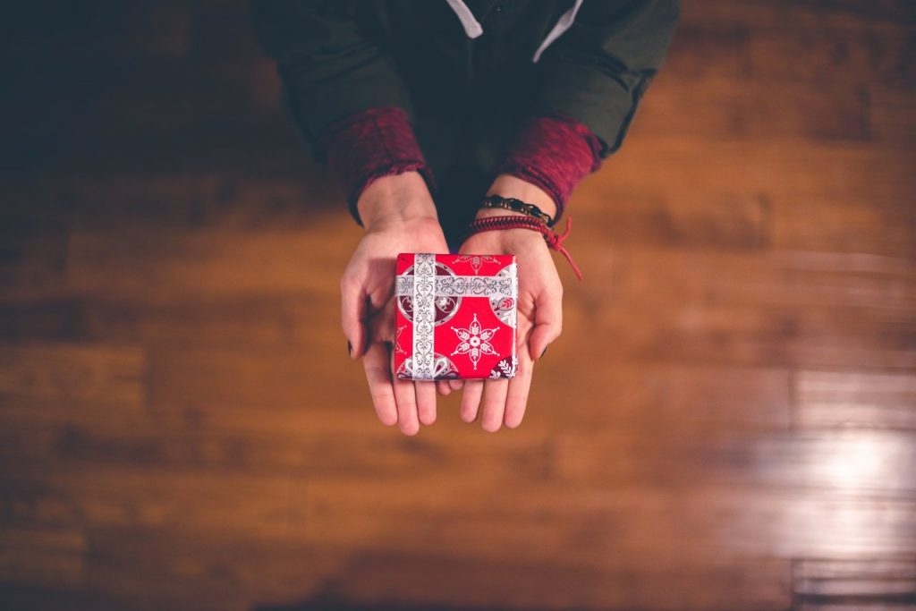 Person holding out a gift for the holidays. Do you have some ideas for holiday gifts?