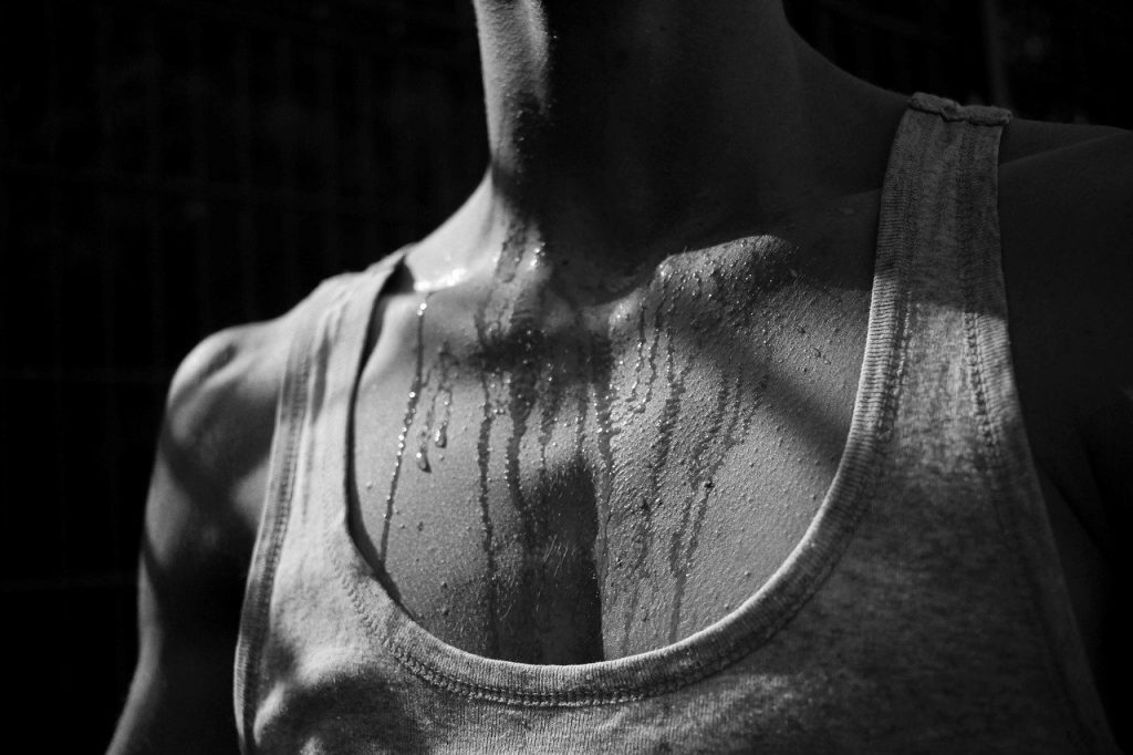 Sweaty man wearing a white tank top. Should you wash your tank tops every time?