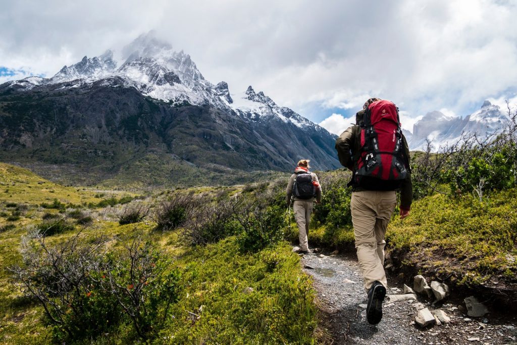 Two people hiking towards a snow covered mountain.
