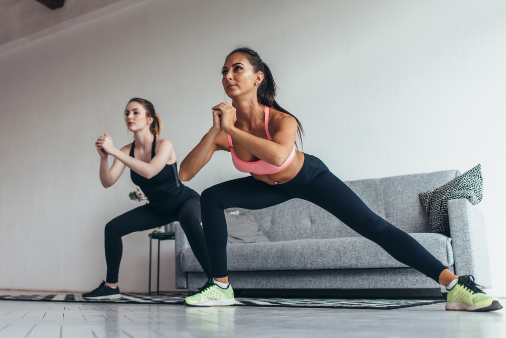 Two women doing lateral lunges at home.