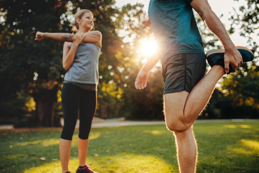Shot of young man and woman stretching in the park. Young couple warming up in morning.