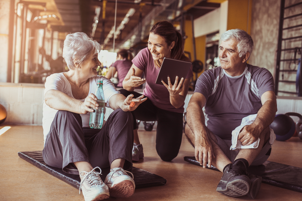 Senior couple in rehabilitation center with personal trainer showing something on digital tablet.