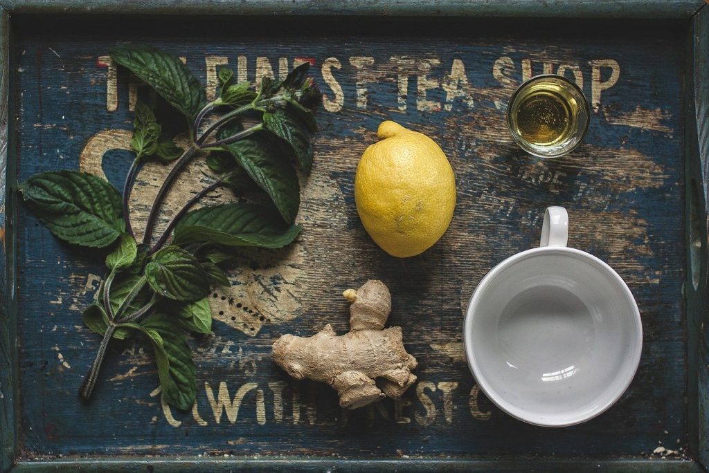 Lemon, ginger, honey, and some greens on a wooden tray.