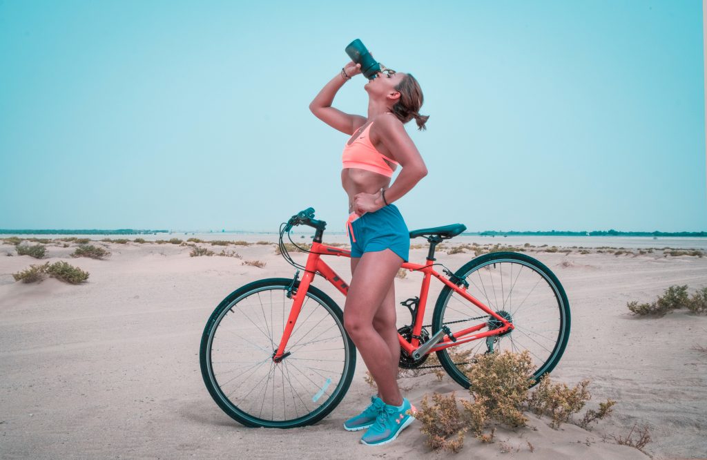 Woman drinking water next to a bicycle.