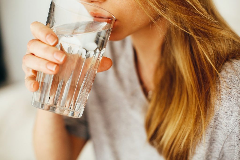 Woman drinking water to stay hydrated and reduce chances of getting muscle knots.