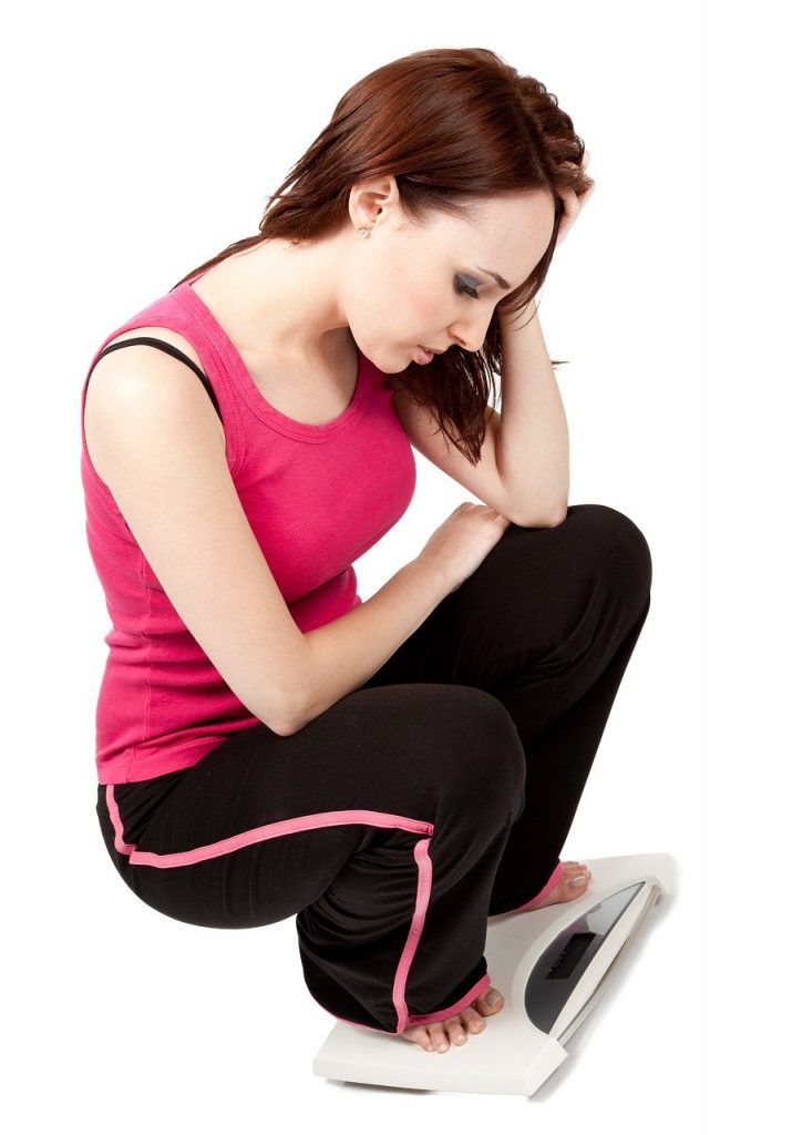 Woman looking upset on a weight scale, probably did not lose weight when she expected to.
