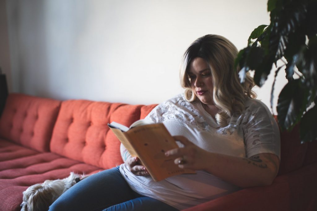 Woman reading a book while sitting on a couch. Too much sitting can cause tight hips, some stretches for hip flexors might be needed.