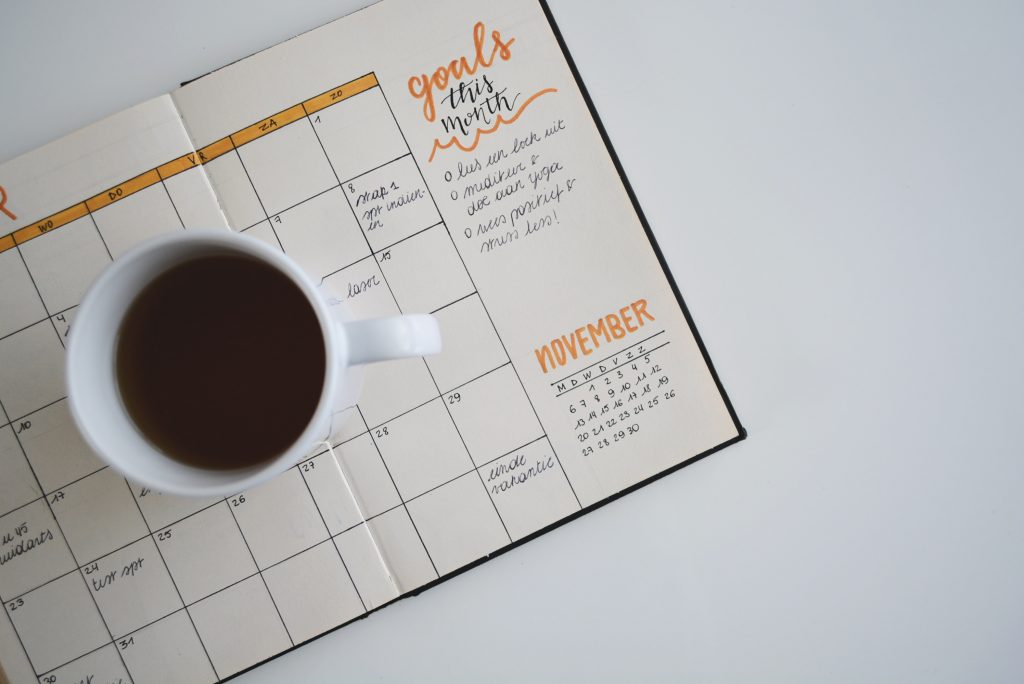 A calendar with notes about goals and a cup of coffee on top of it.