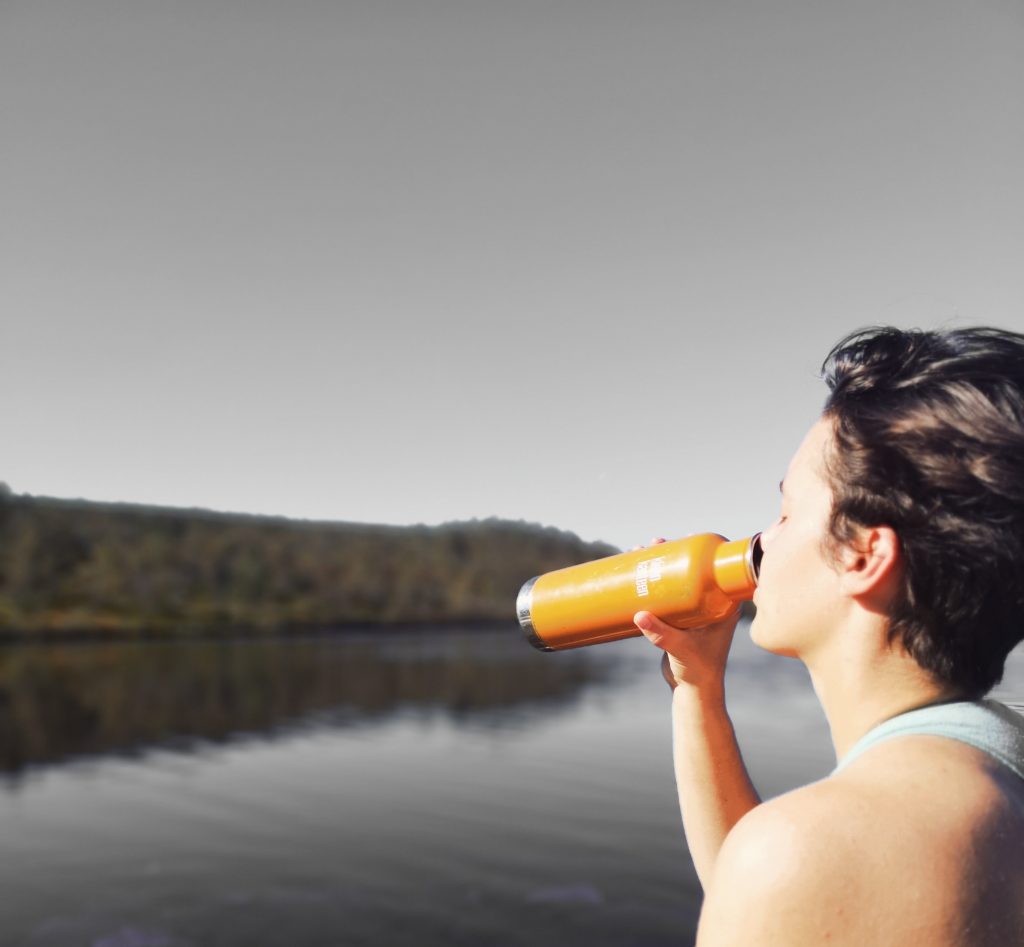Person drinking water by the lake. Drinking enough water is one of the tips on how to boost metabolism.