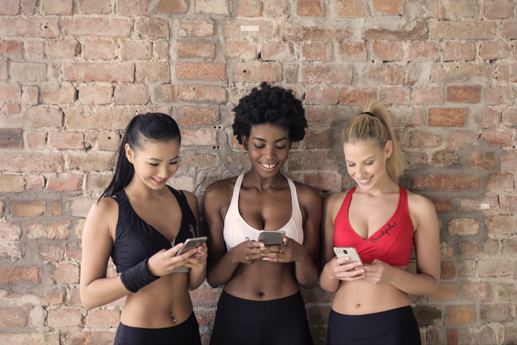 Three women looking at best fitness apps on their phone before working out.