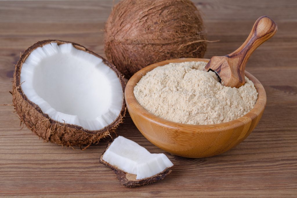 Coconut flour in a wooden bowl, next to a couple of coconuts.