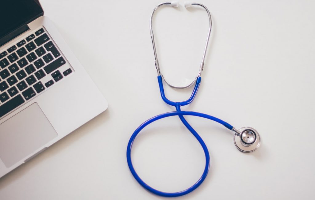 Stethoscope next to a laptop on a desk.