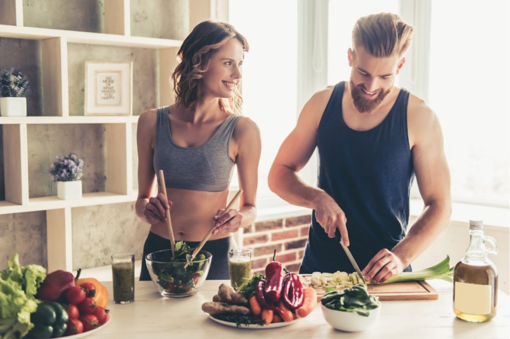 A man and woman enjoying cooking a vegetable dish together.