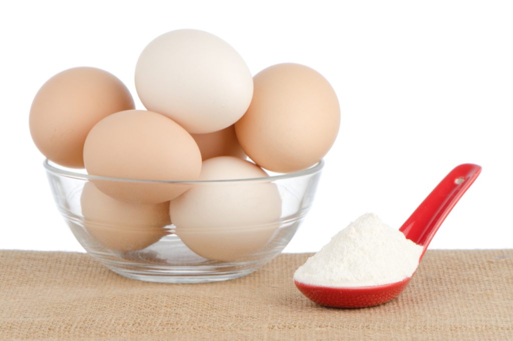 Eggs in a clear glass bowl next to a spoonful of white powder.