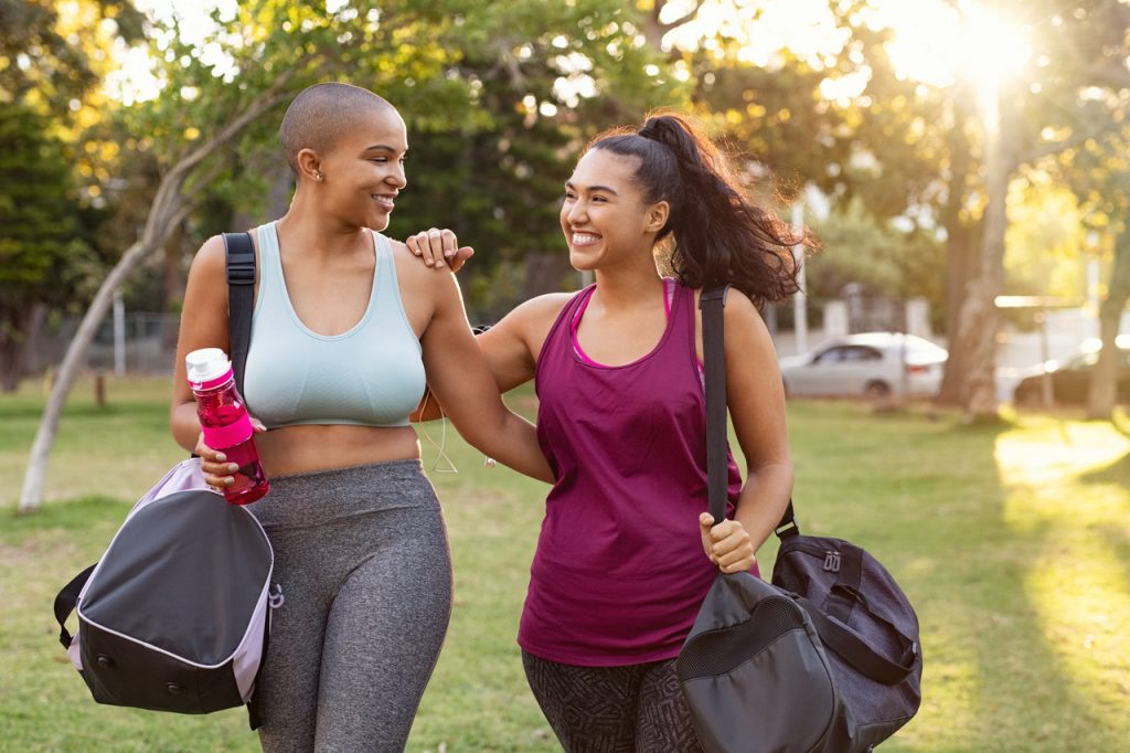 Friends looking happy while walking together, holding gym bags.