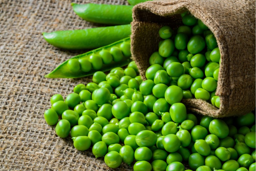 A bag of peas and some peapods on a cloth surface.