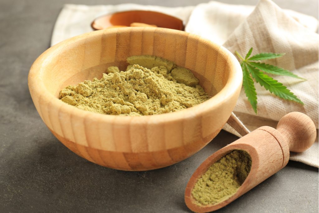 Hemp protein powder in a wooden bowl with a leaf of cannabis on the side.
