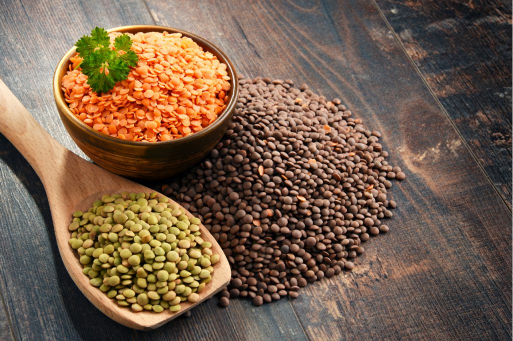 Different types of protein-rich lentils, in a bow, in a wooden spoon and on a wooden table.