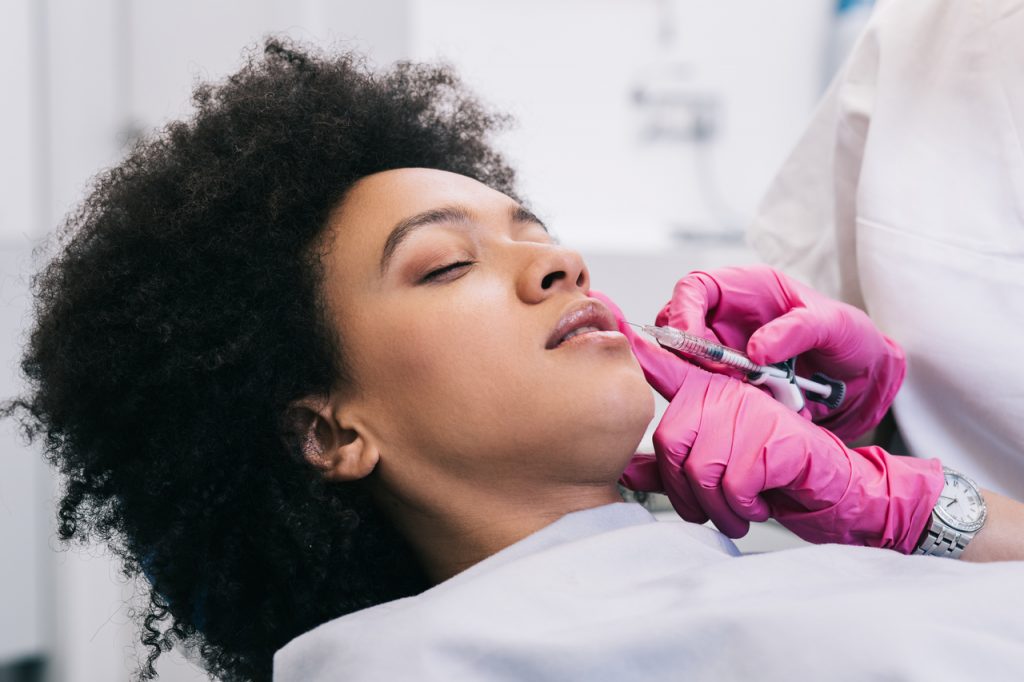 Close up of beautician expert's hands injecting botox in female lips.