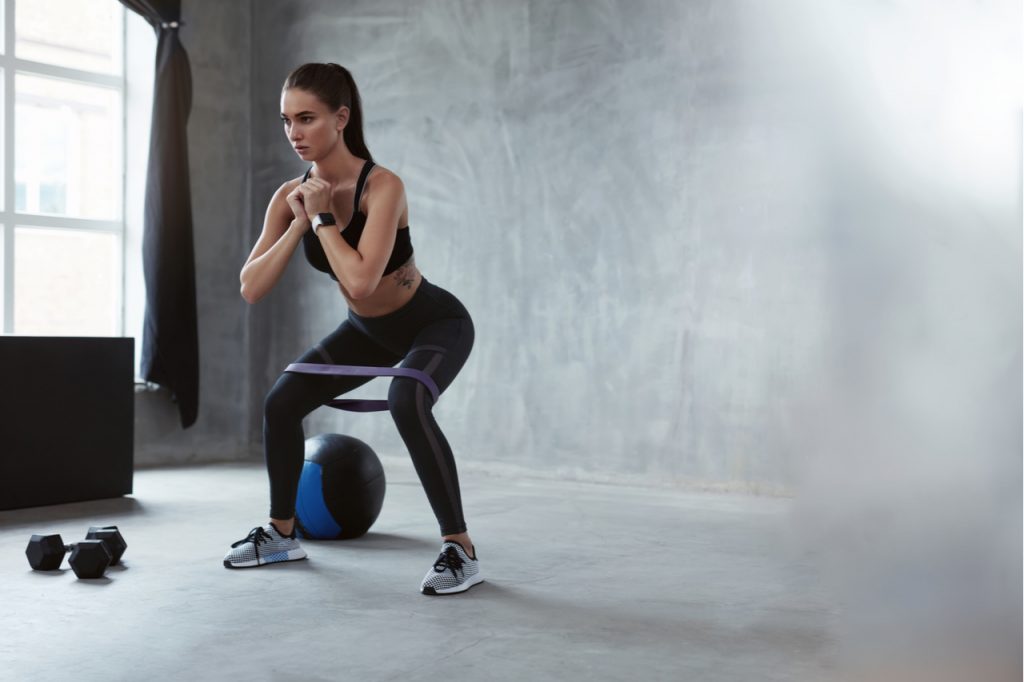 A woman using a resistance band while squatting side to side.