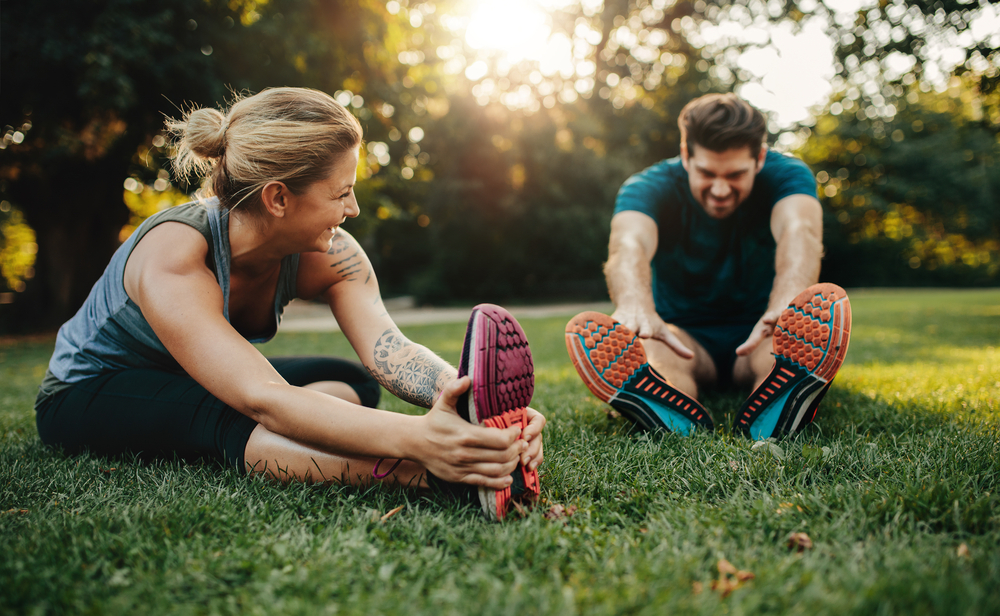 A man and woman doing stretching while taking advantage of the mental health benefits of nature.