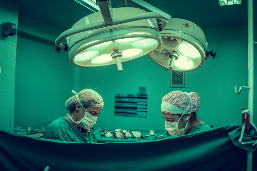 Two people behind a curtain in surgery room performing lip augmentation surgery.