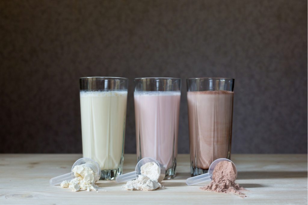 Three glasses of protein shakes with different flavors, vanilla, strawberry, and chocolate. Showing different types of protein powder.