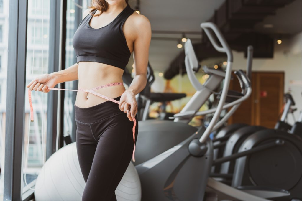 A woman checking her trifecta meal plan diet results using a tape measure after a workout.