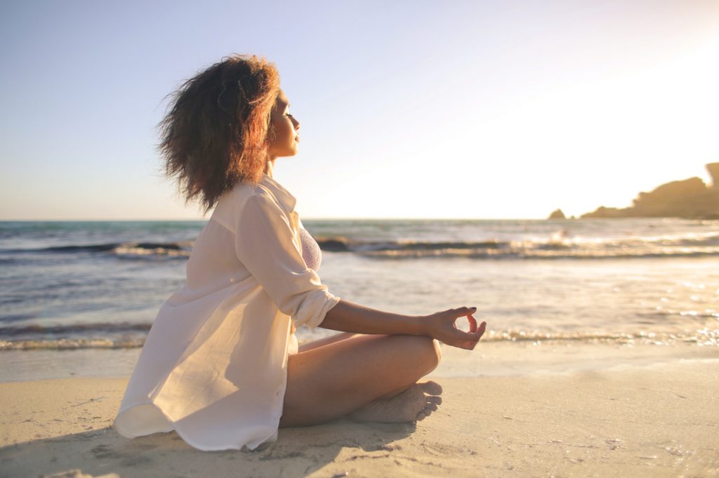 A woman doing yoga at the beach with white sand.