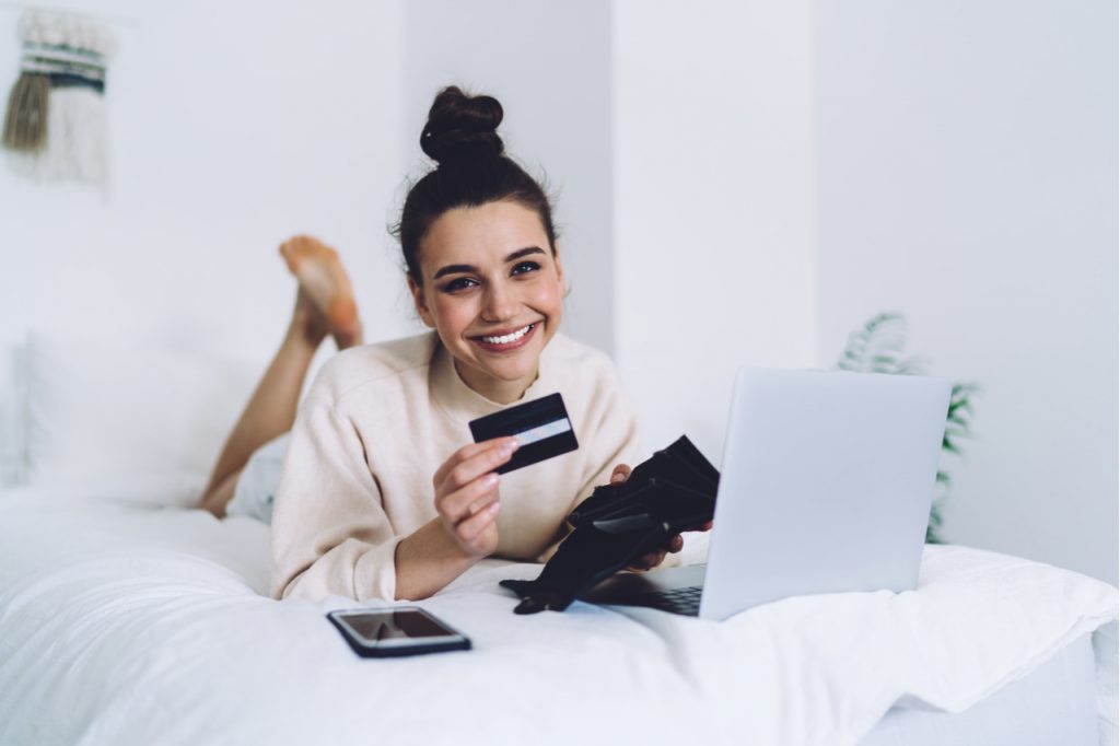 Woman holding credit card and wallet in bed, budgeting as her morning ritual.