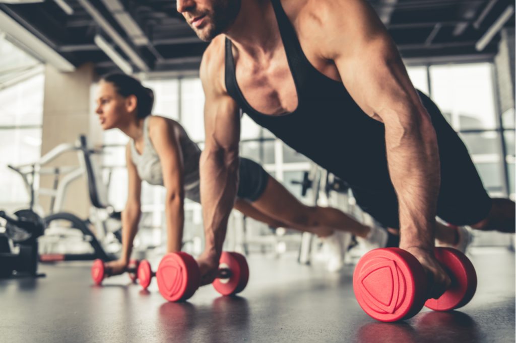 A man and woman doing a dumbbell exercise who will need tips on relief for muscle soreness.