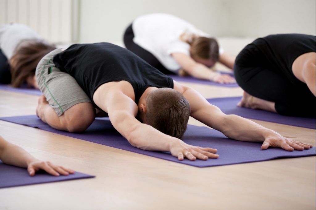 A man doing the child pose restorative yoga with a group.