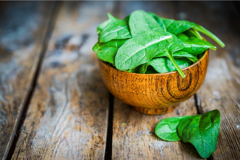 A bowl of fresh spinach in a wooden table.