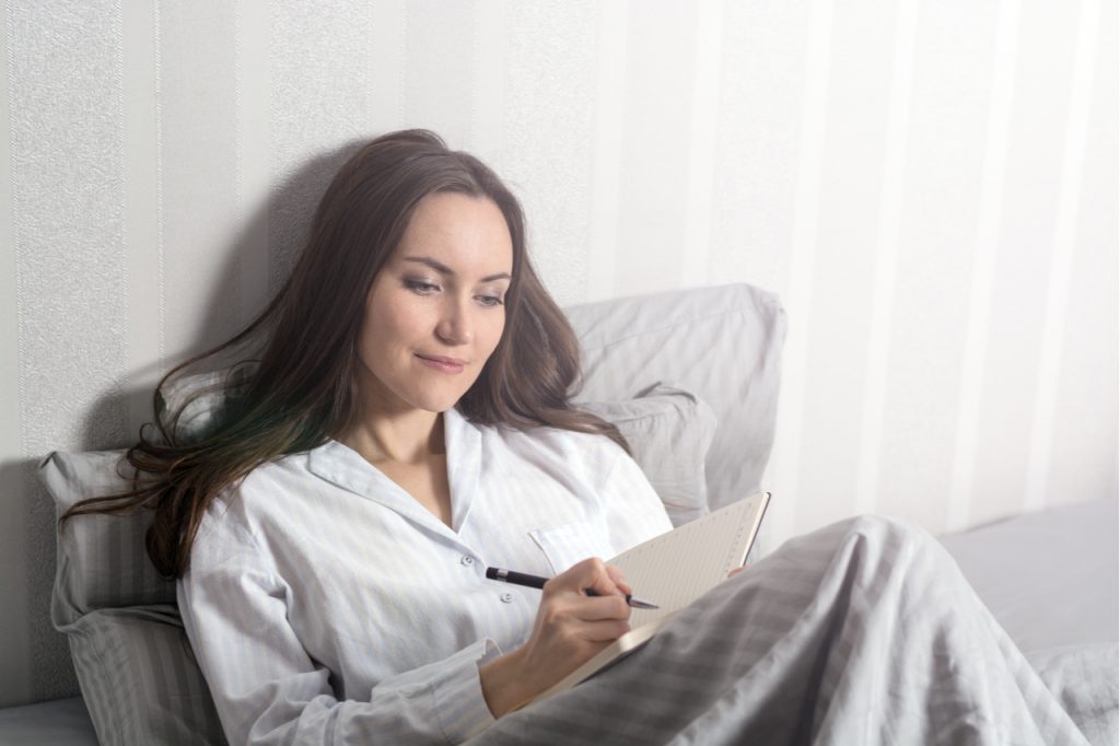 Woman writing on her journal in bed after waking up.