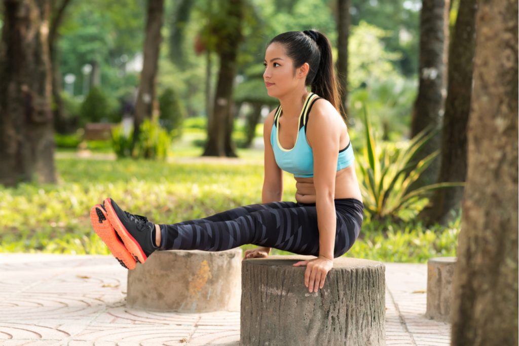 A woman doing the L-sit exercise to stay fit in a park,