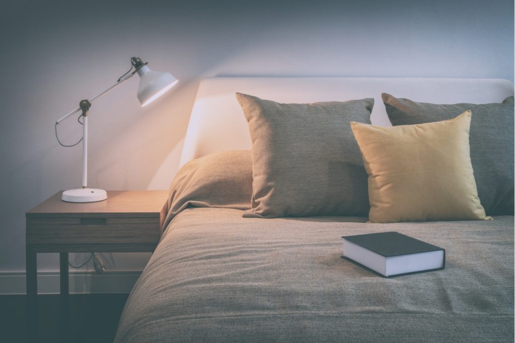 An image of a comfortable bed with a book to ready before bedtime.